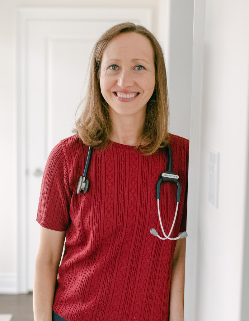 Dr. Lizete smiling, standing in a doorway with a stethoscope.